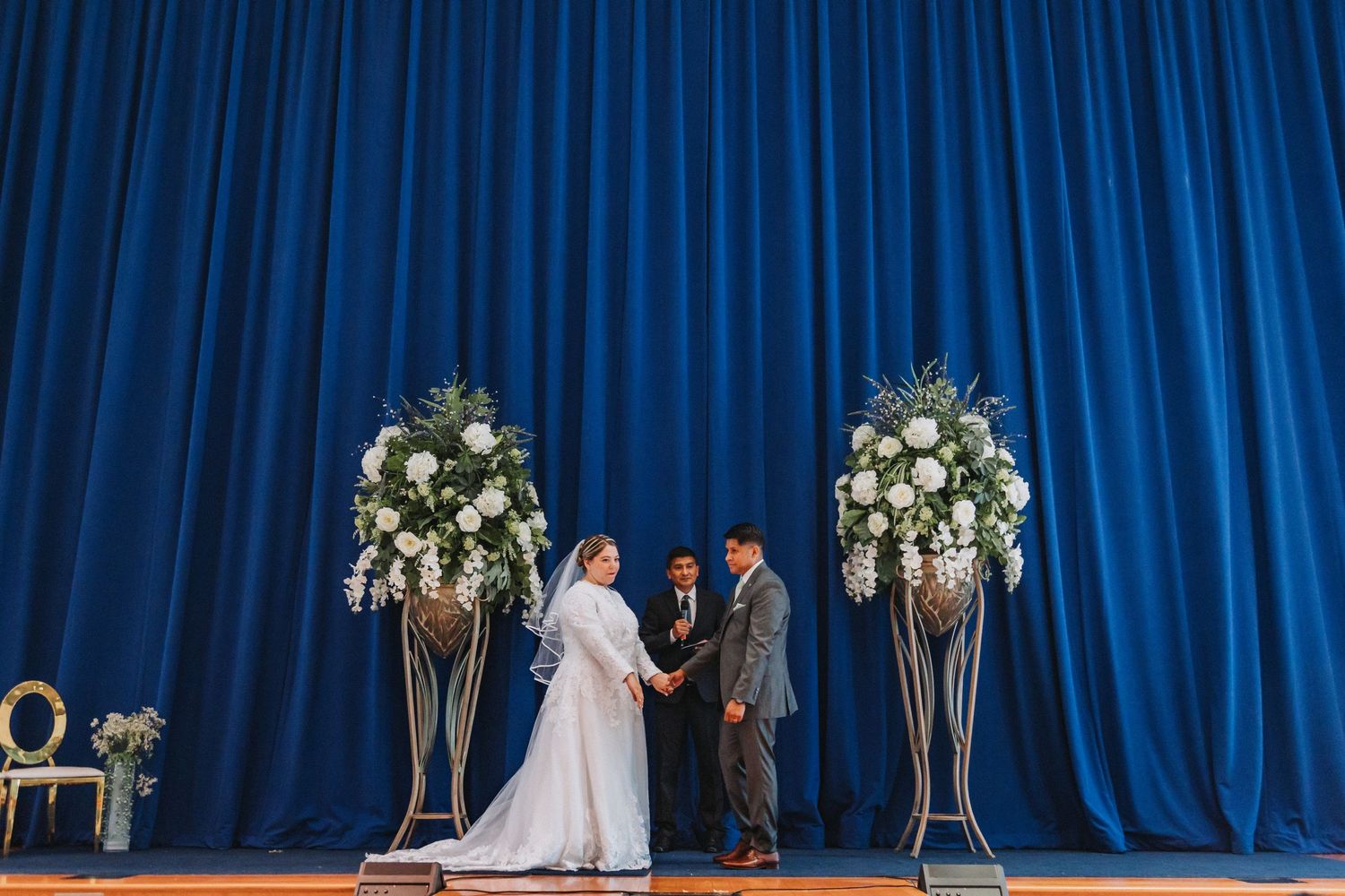Wedding ceremony setup with blue curtain backdrop and floral arrangements on pedestals.