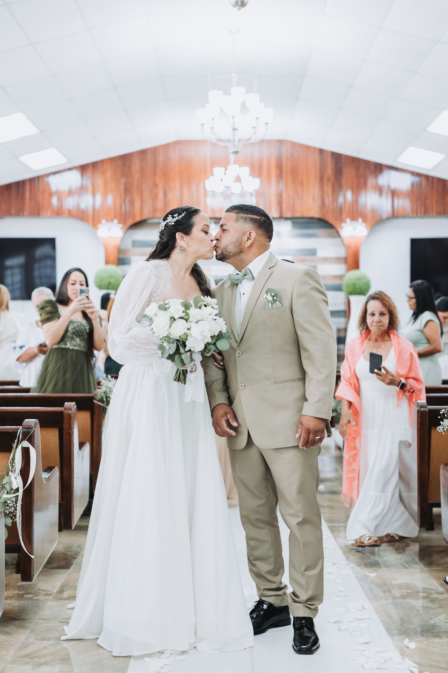 Wedding ceremony inside a chapel with white aisle runner and wooden pews.