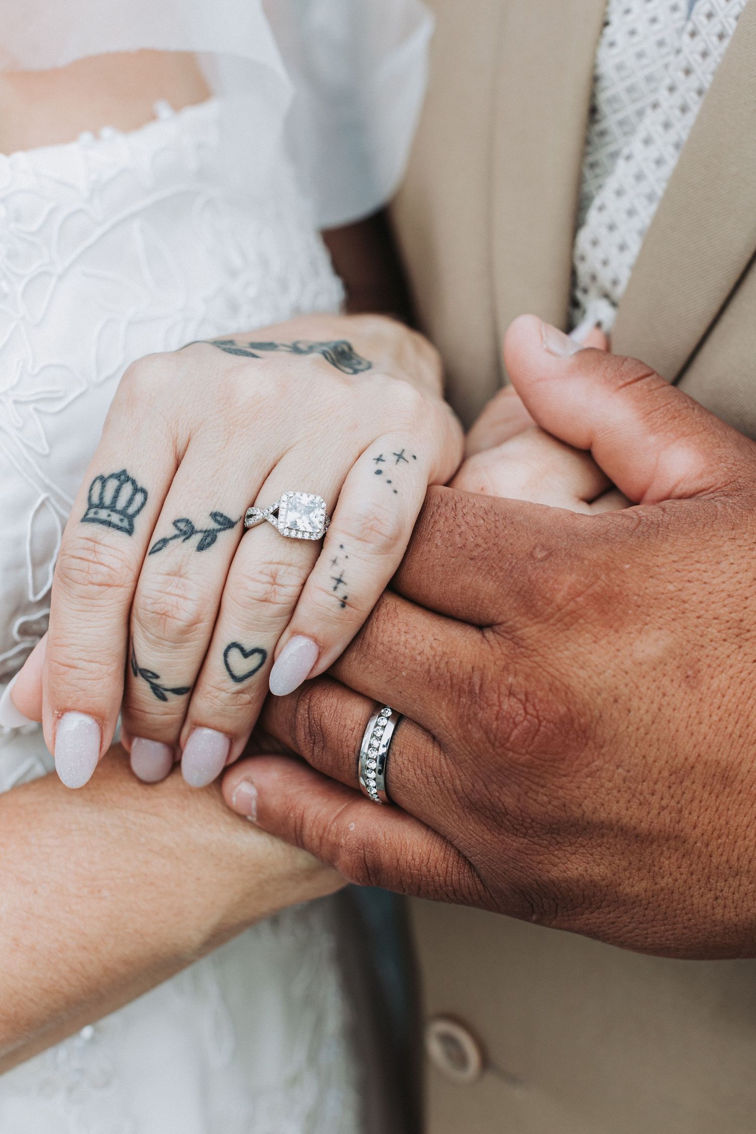 Close-up of wedding rings and tattooed hands showing intimate moment.