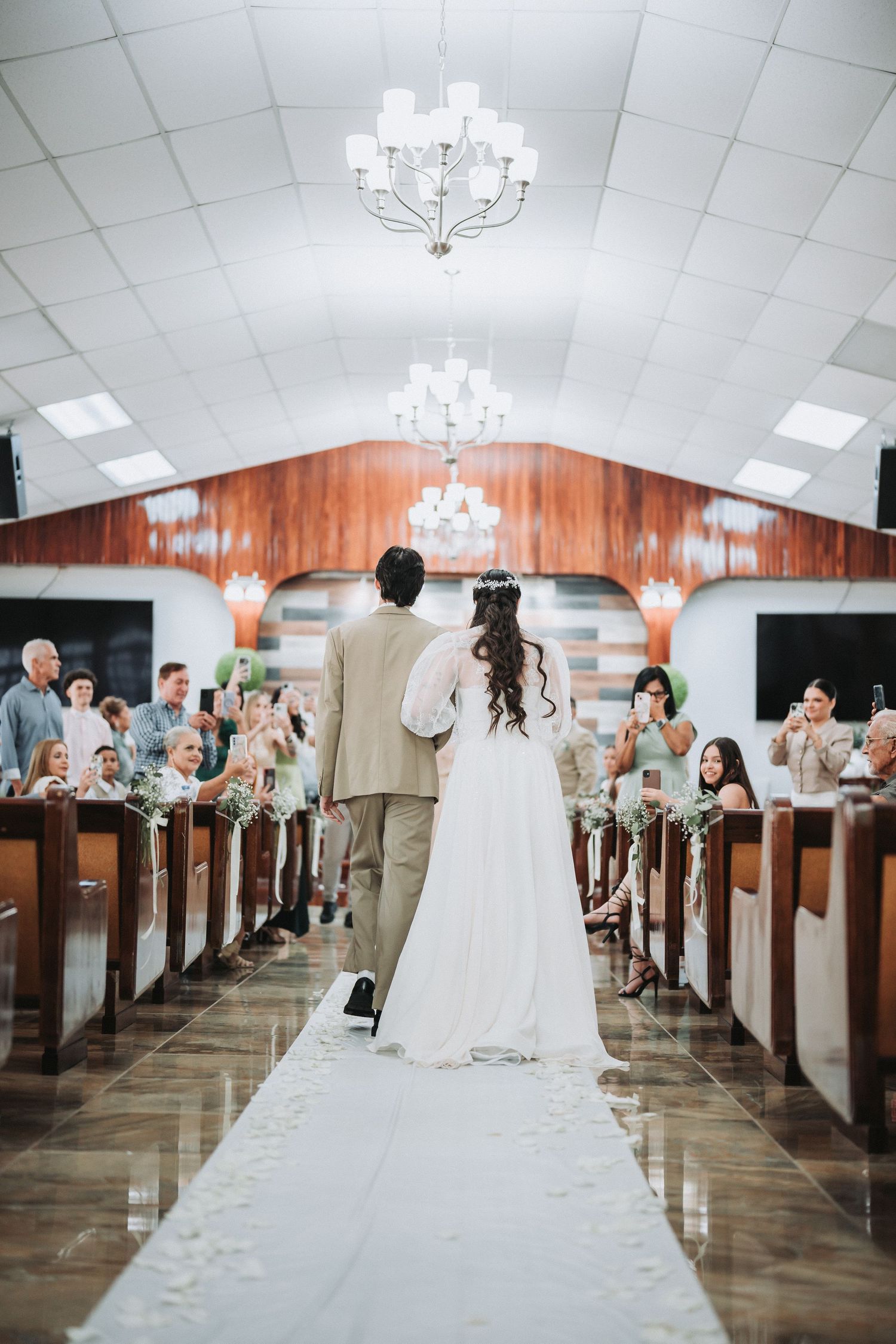 Wedding ceremony in a church with wooden pews and chandeliers.
