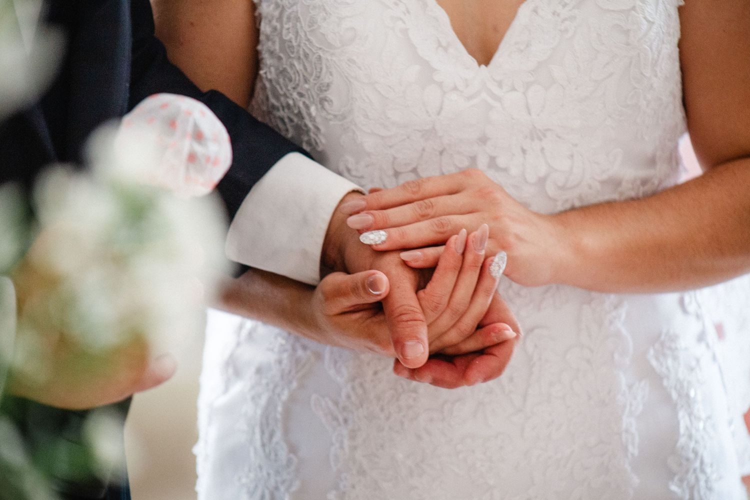 Close-up of bride and groom holding hands, showcasing wedding rings on their special day.