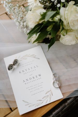 Elegant wedding invitation with white floral design lies next to rings and white roses