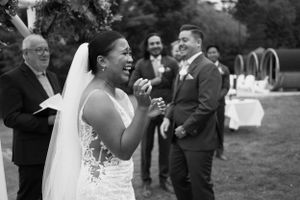 A bride in a white lace wedding dress laughs joyfully during an outdoor garden reception.