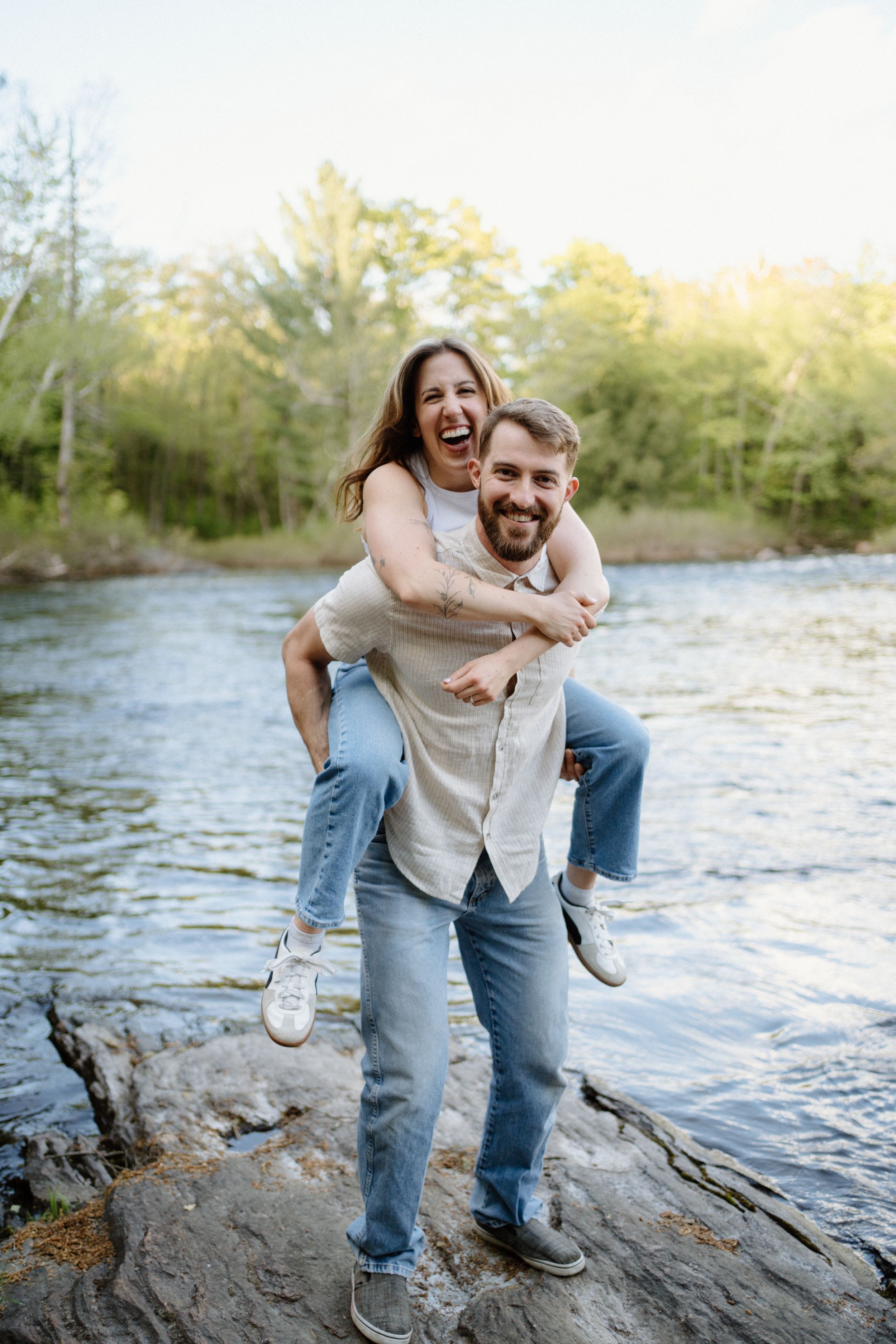 Engagement photo of a laughing couple on rocks by the Oxongue river-Alexis Anne Photography-Muskoka wedding photographer