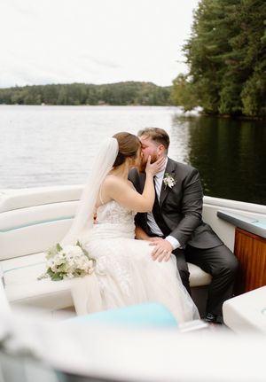 Romantic wedding couple sharing intimate moments on a boat with scenic lake and forest views in the background.