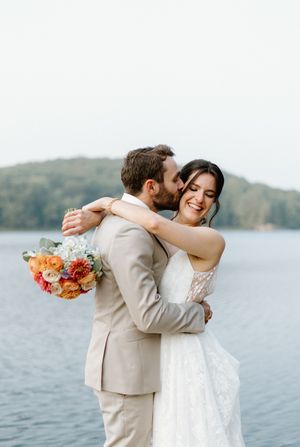 Couple embraces by a lakeside, with the bride holding a beautiful bouquet-Cottage Country flowers-trillium Resort-Alexis Anne Photography