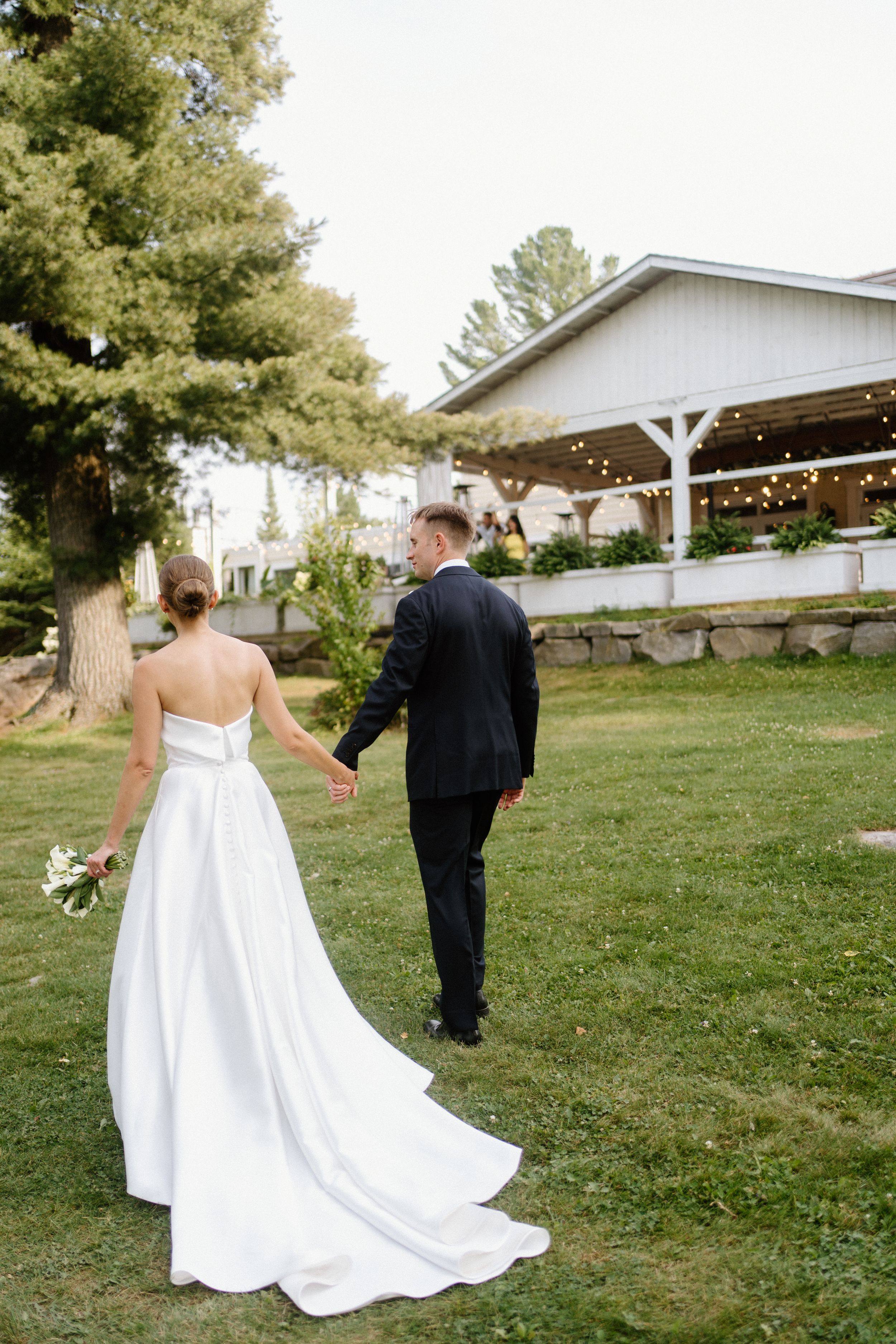 Couple hand in hand walk across the lawn Northridge Inn  the background-Alexis Anne Photography-Luxury Wedding Photographer for Muskoka