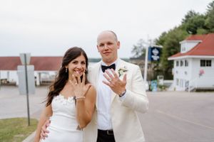 Newlyweds in wedding attire show off their rings while standing on a street in front of Windermere House in Muskoka-Alexis Anne Photography