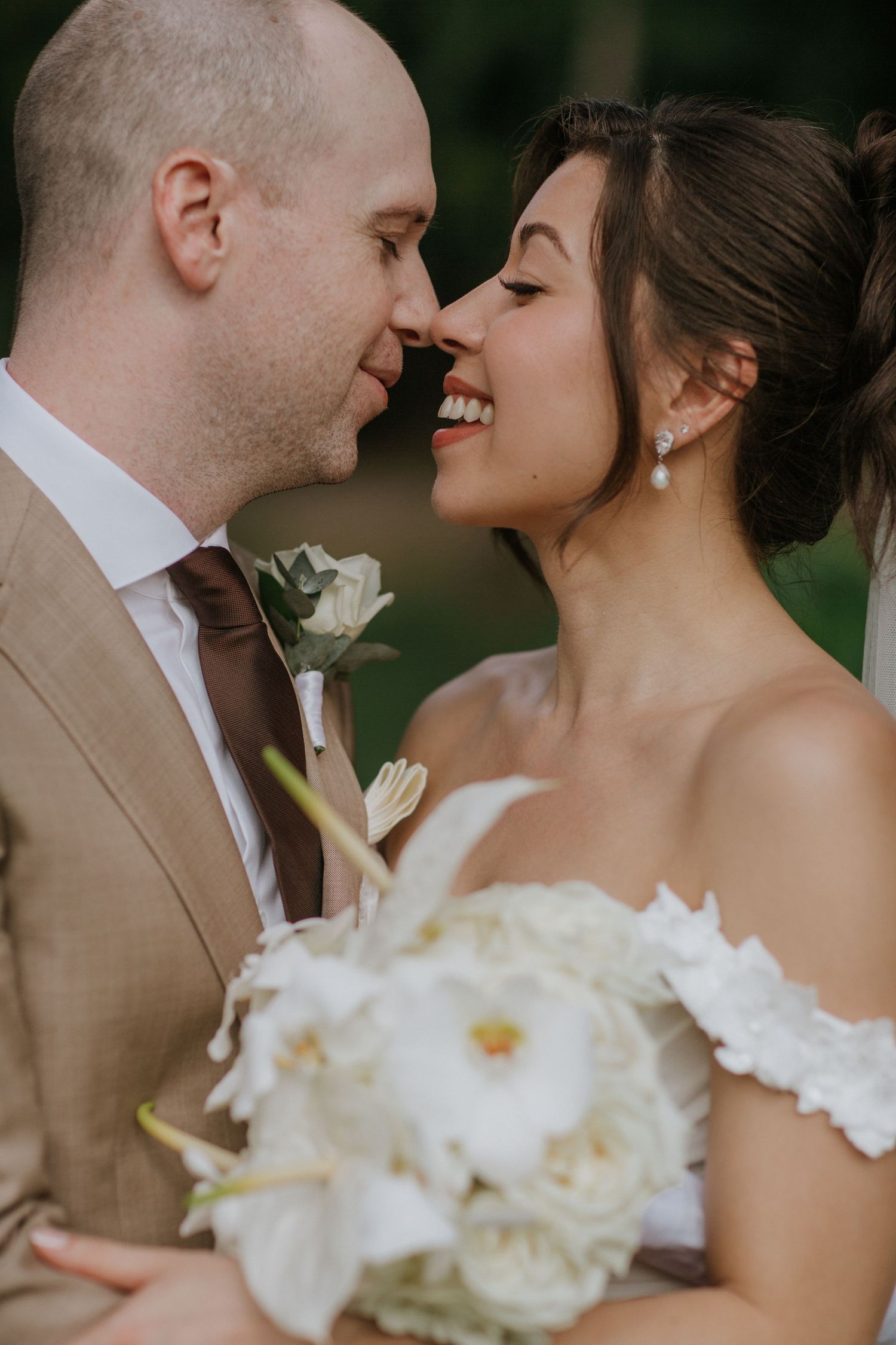A romantic wedding couple shares an intimate moment with white flowers in the foreground.