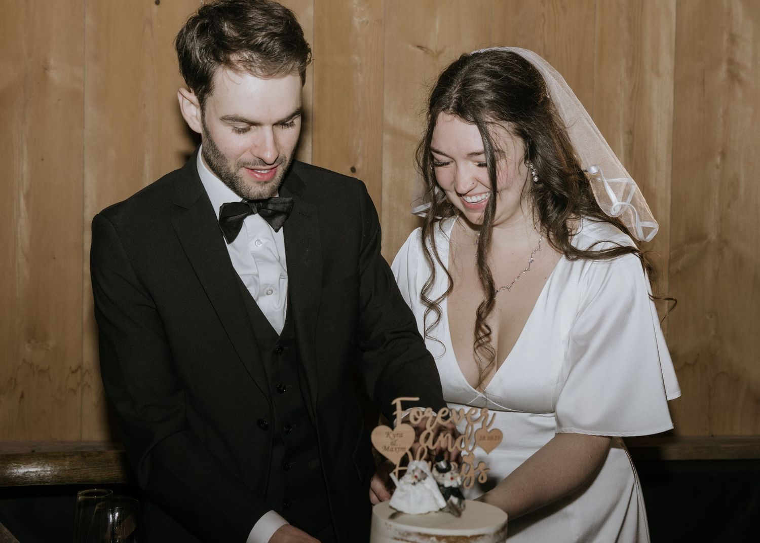 Newlywed couple signs marriage documents together at a rustic wooden venue.