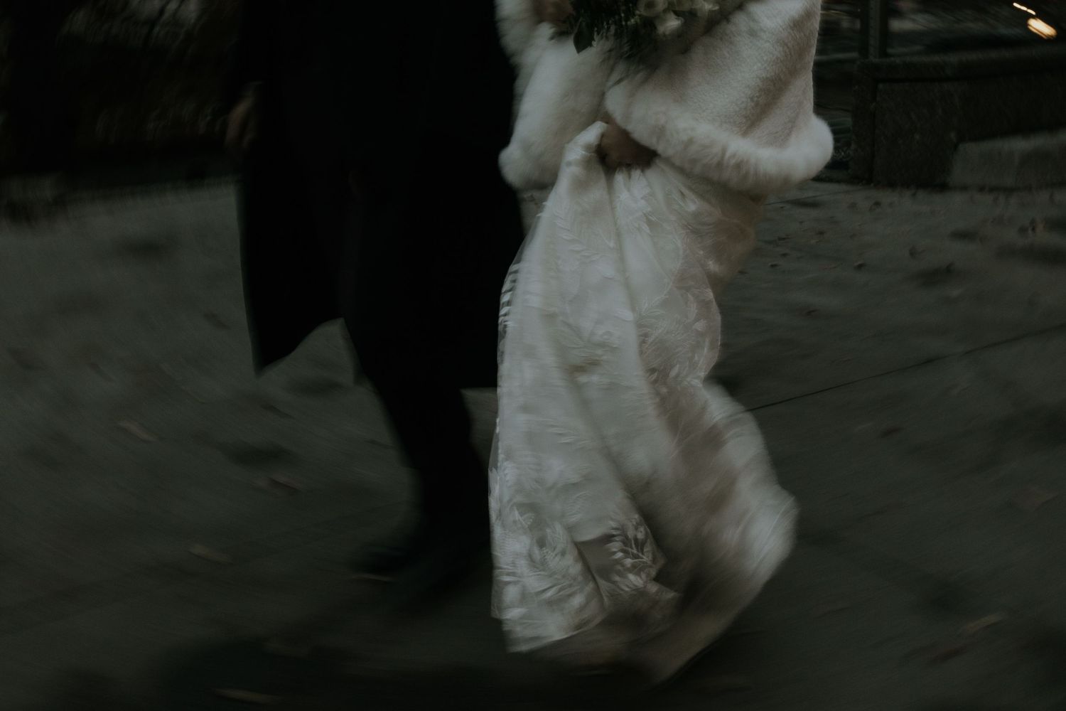 A bride in a white wedding dress walks down a dark hallway with her dress trailing behind her.