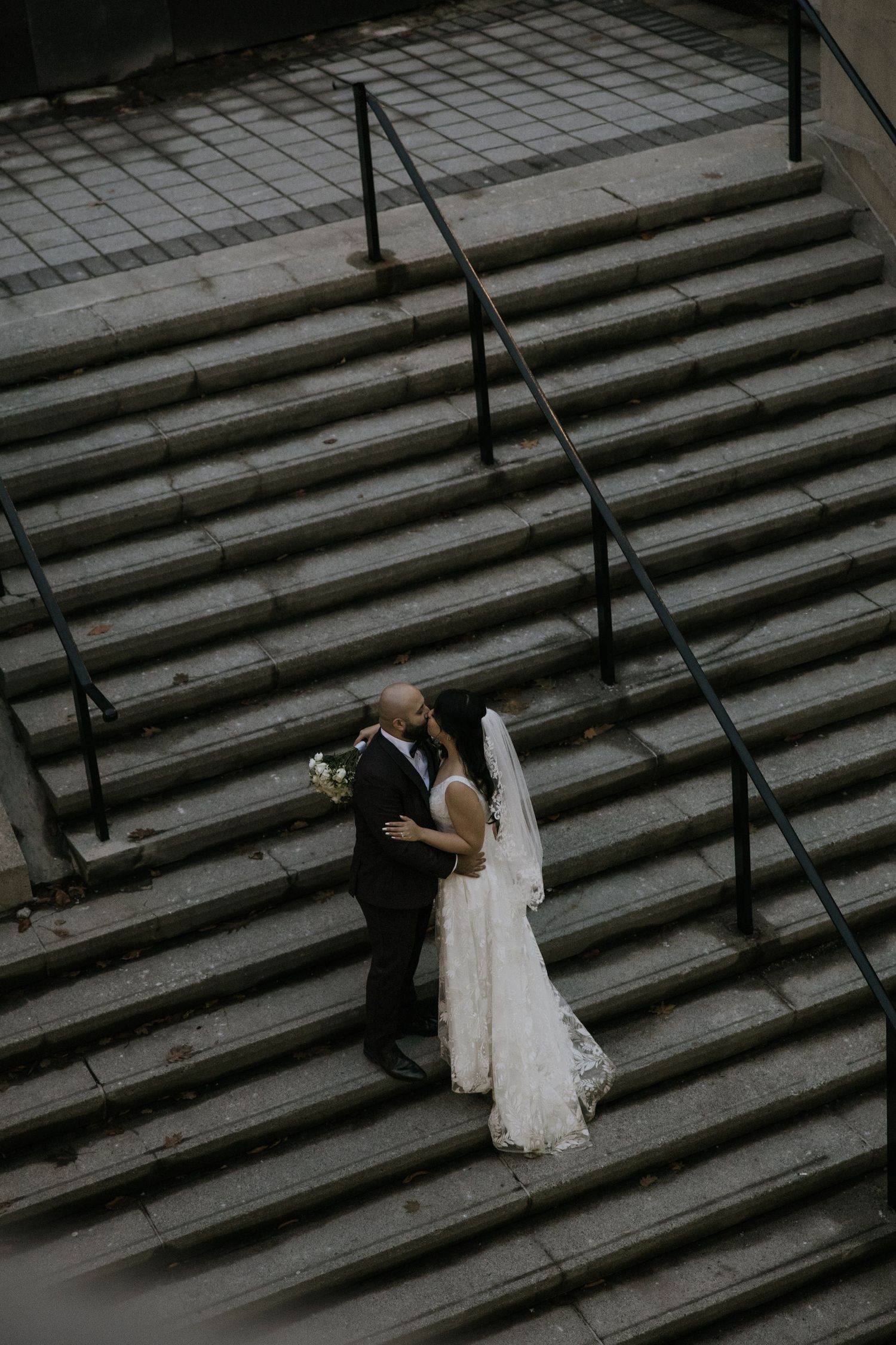 A couple shares a romantic moment on grand stone steps, with the bride wearing a flowing white gown and veil.