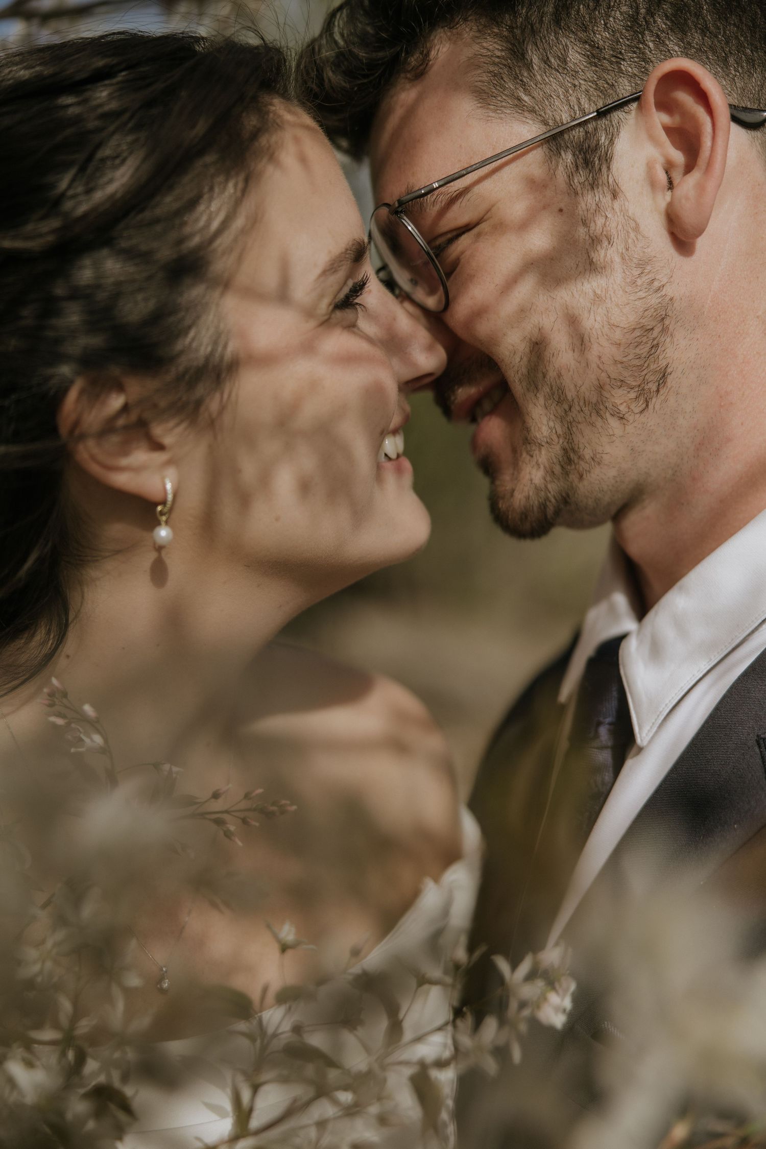 Intimate wedding portrait captured through delicate foliage showing a tender romantic moment between newlyweds.