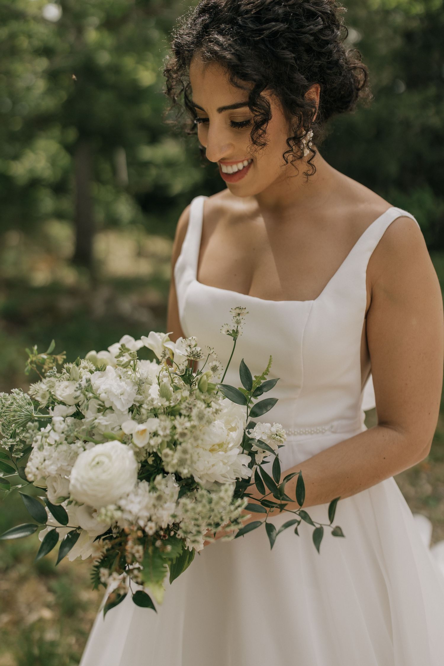 A beautiful white bridal bouquet with roses and delicate greenery against a wedding dress.