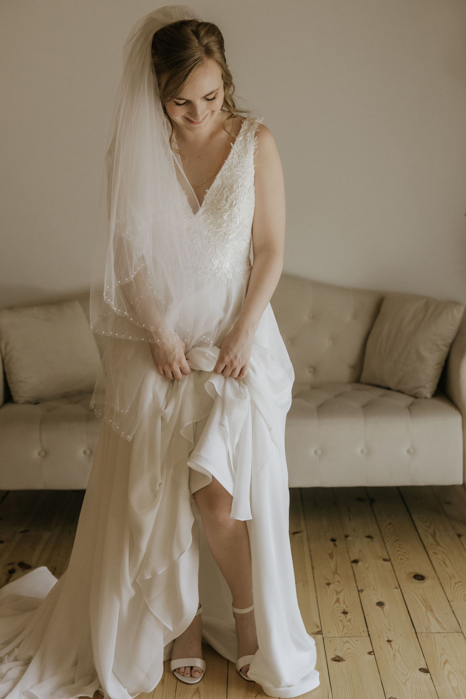 A bride in a flowing white wedding dress and veil prepares for her special day on a wooden floor.