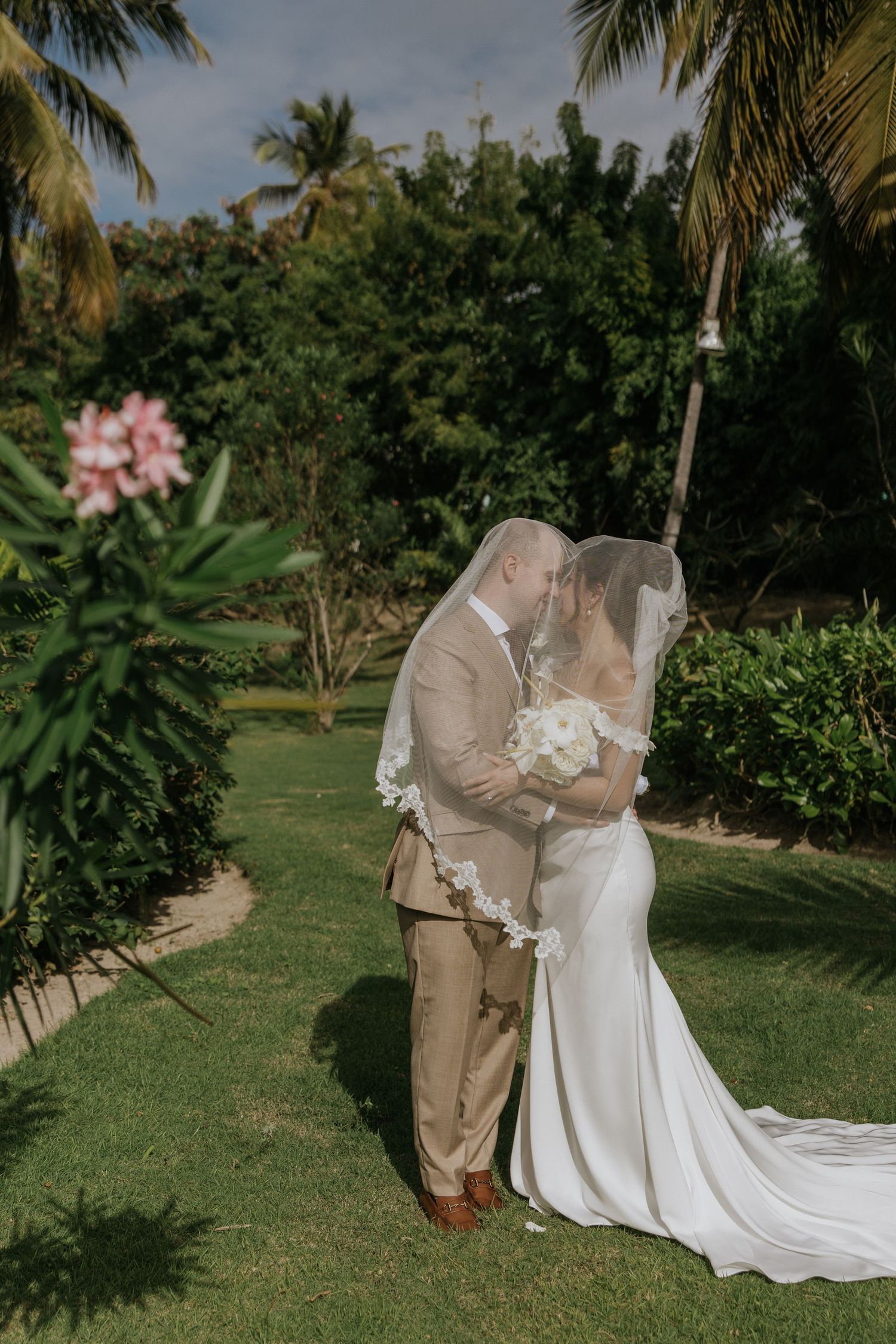 A couple shares an intimate moment during their tropical garden wedding ceremony surrounded by palm trees and lush greenery.