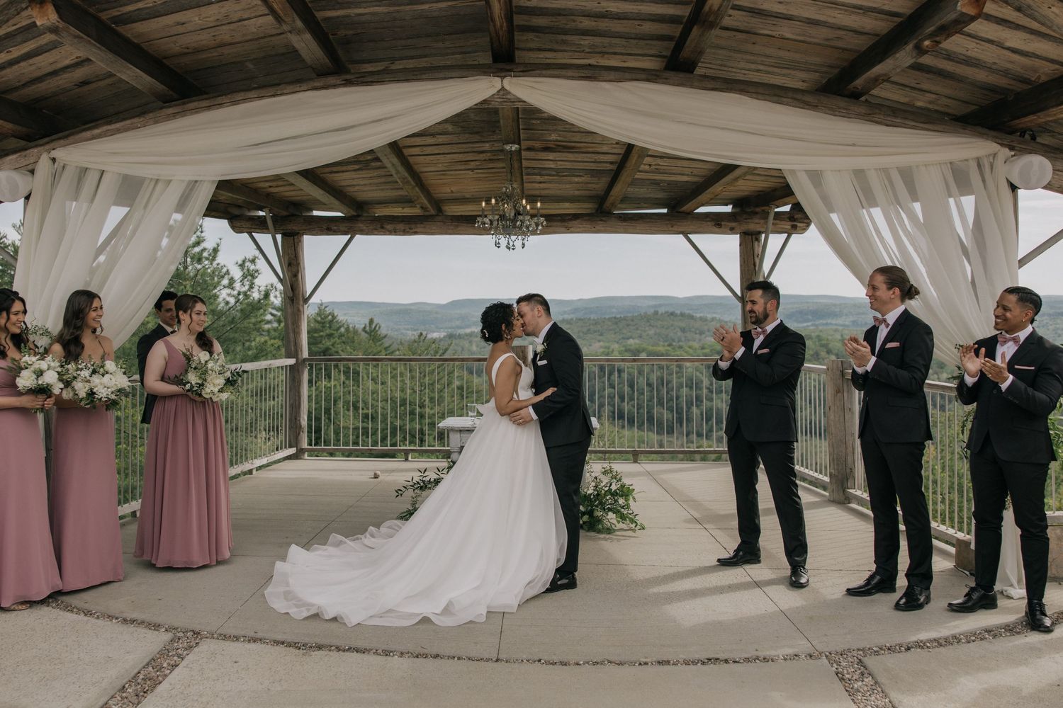 Elegant outdoor wedding ceremony set against a mountain backdrop with stone pillars and white draping.