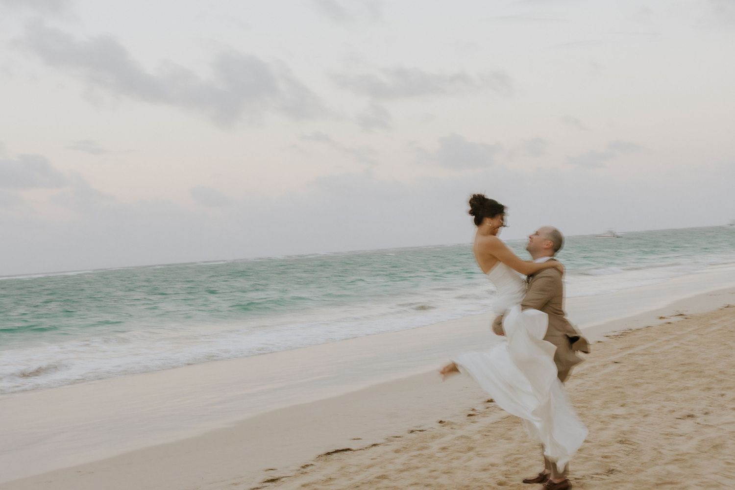 A romantic beach photoshoot sequence showing a couple walking and embracing along a sandy shoreline at sunset.