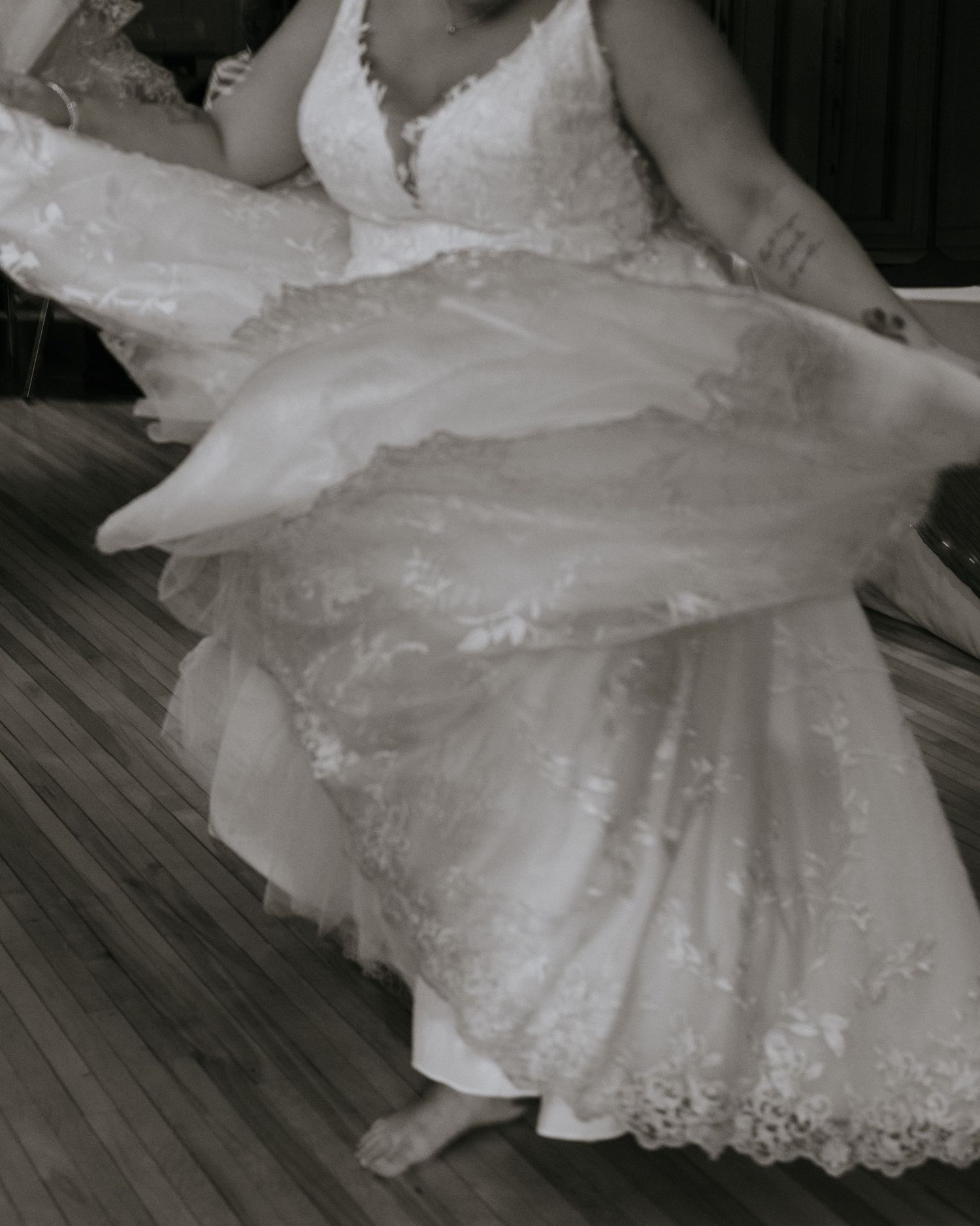 A wedding dress with intricate lace details and a flowing white skirt is displayed on a wooden floor.