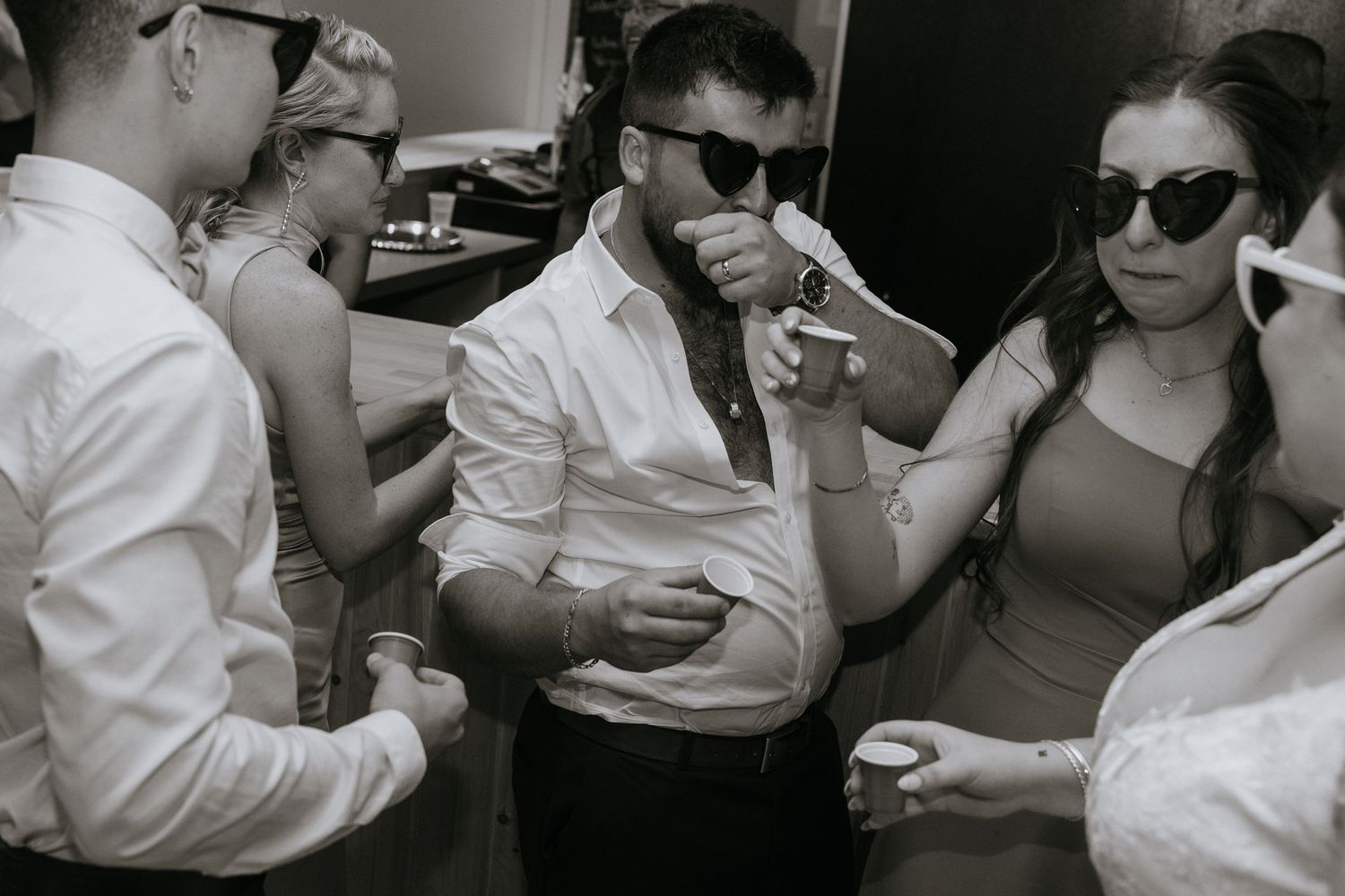 A black and white photograph of people in sunglasses drinking coffee and smoking outdoors.