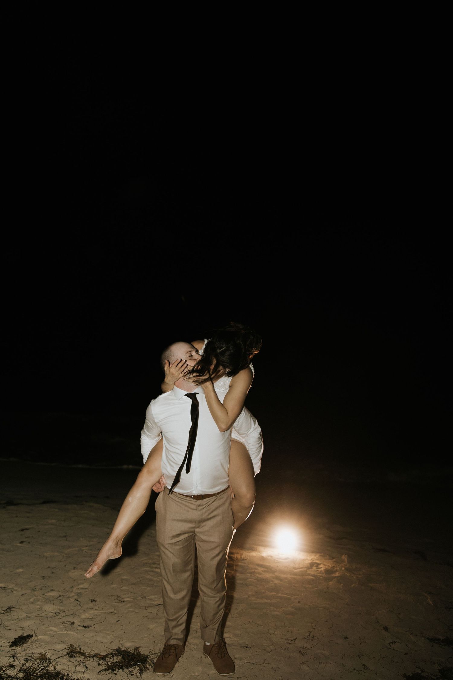 A person in casual attire holds a sparkler on a dark beach at night creating a glowing light trail effect.