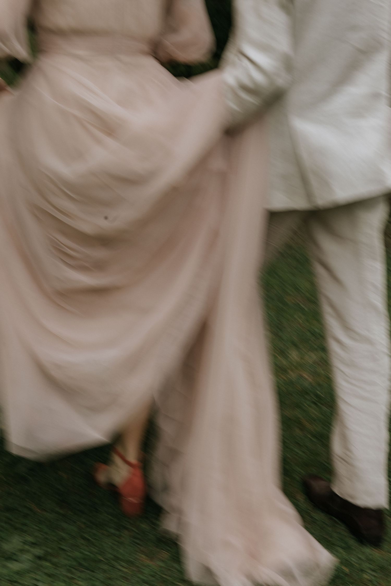 An artistic close-up of flowing blush pink and white formal attire against green grass.
