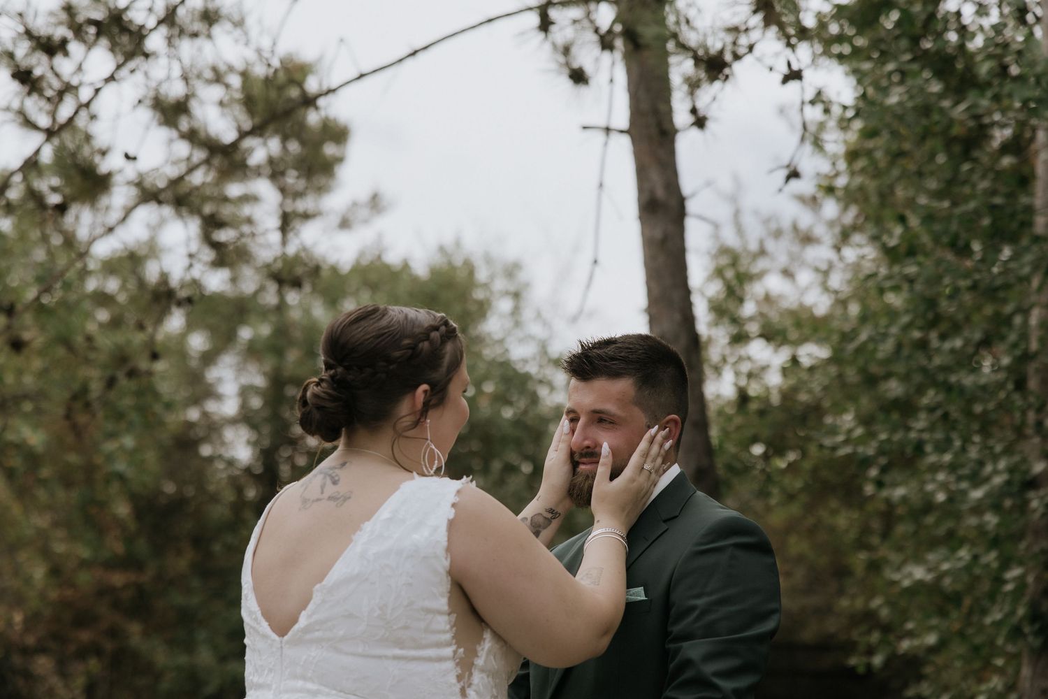 A couple shares an intimate moment outdoors surrounded by tall pine trees and greenery.