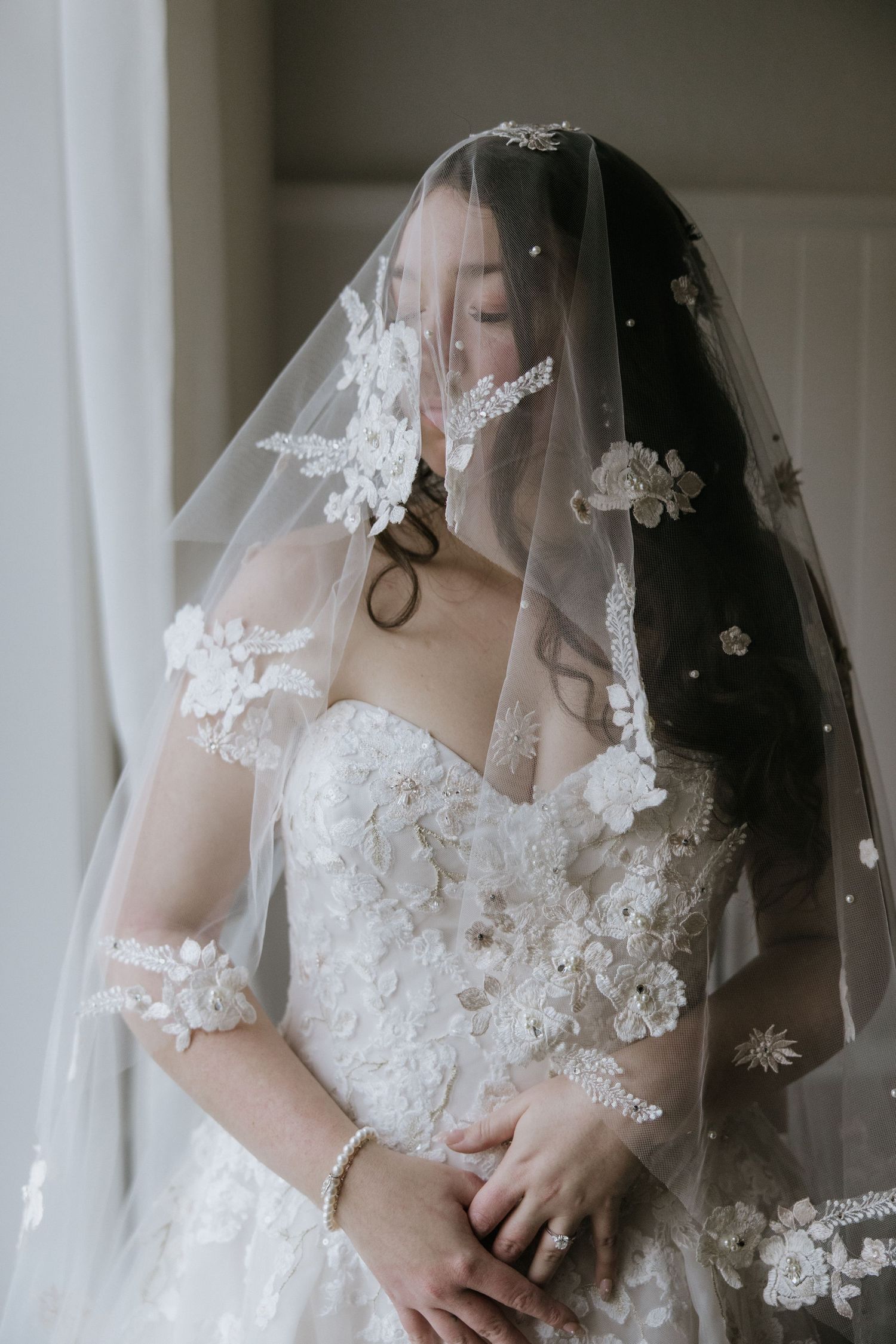 A delicate lace wedding veil drapes elegantly over a bride wearing an ornate white gown with floral appliques.