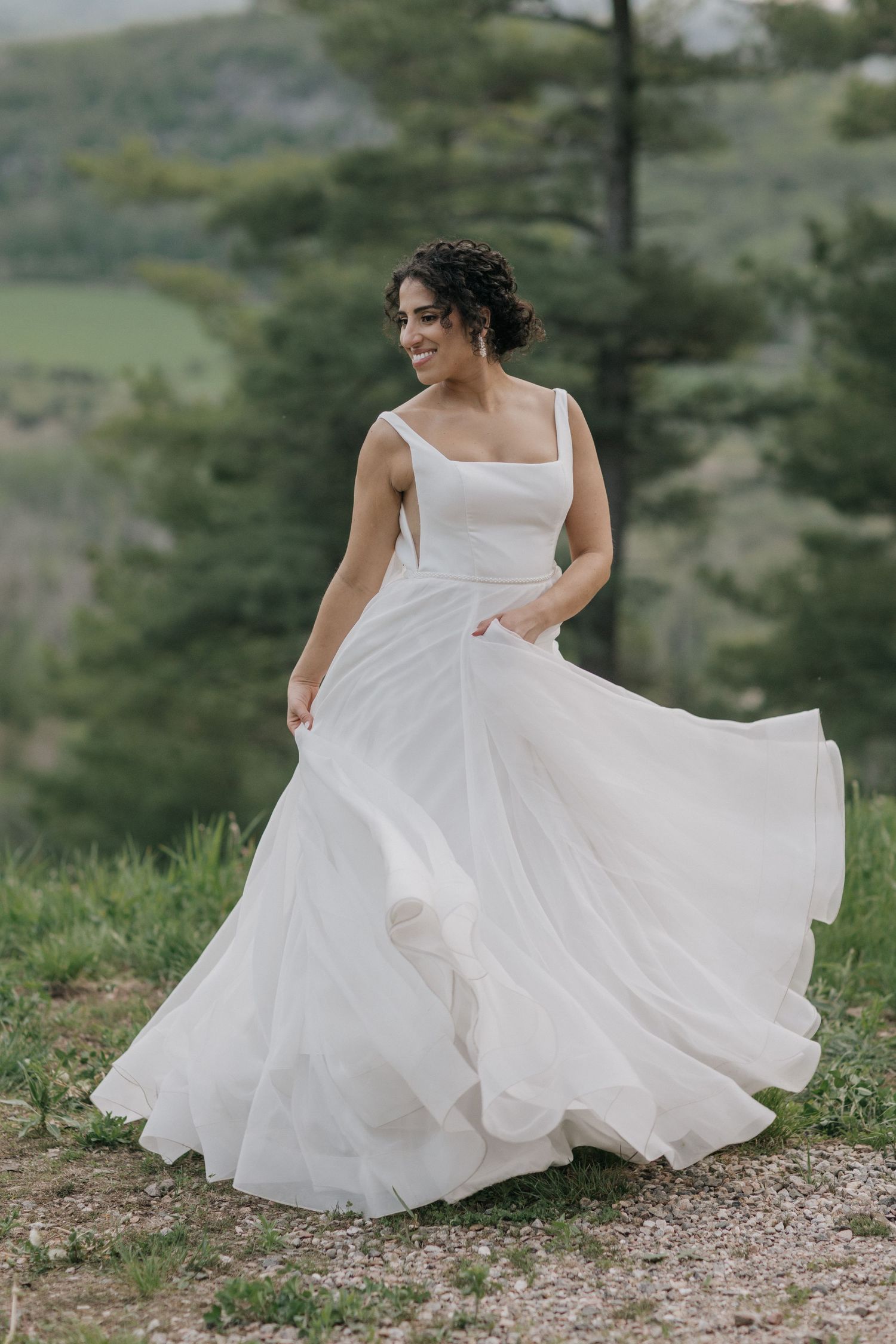 Bride in flowing white gown twirls on mountain peak with dramatic landscape views.