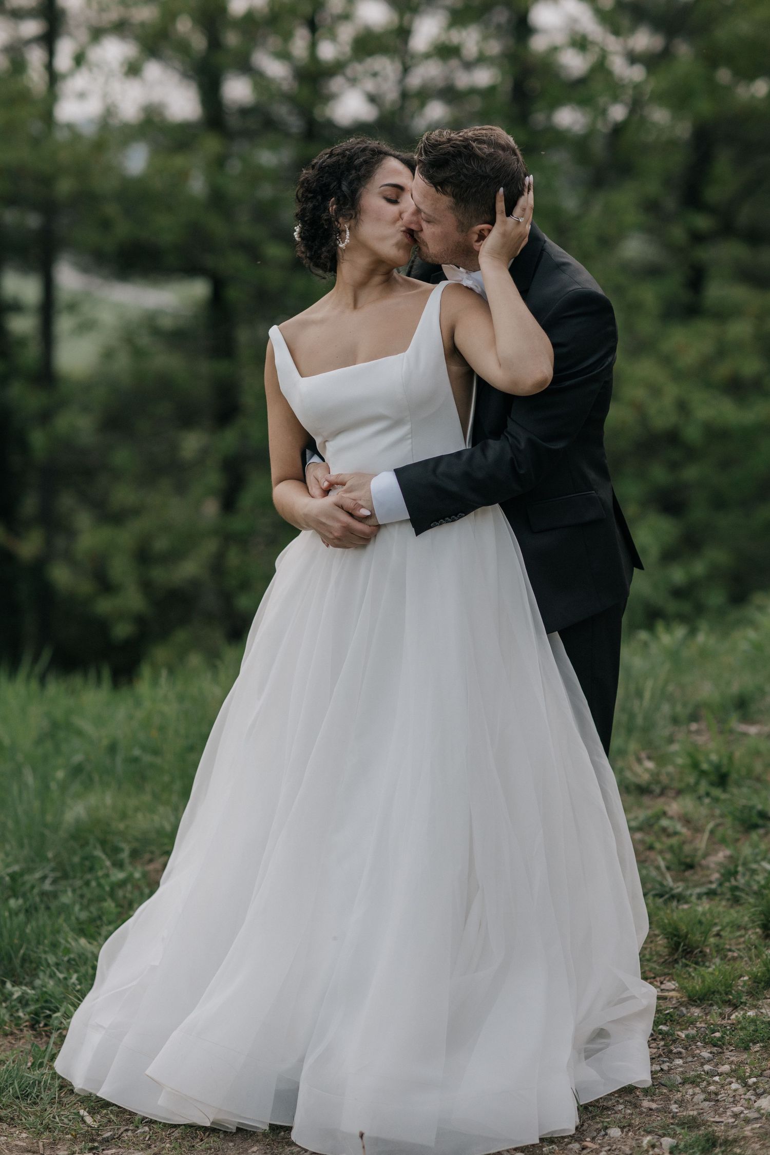 Romantic moments captured between newlyweds in white dress and black suit on mountain terrain.