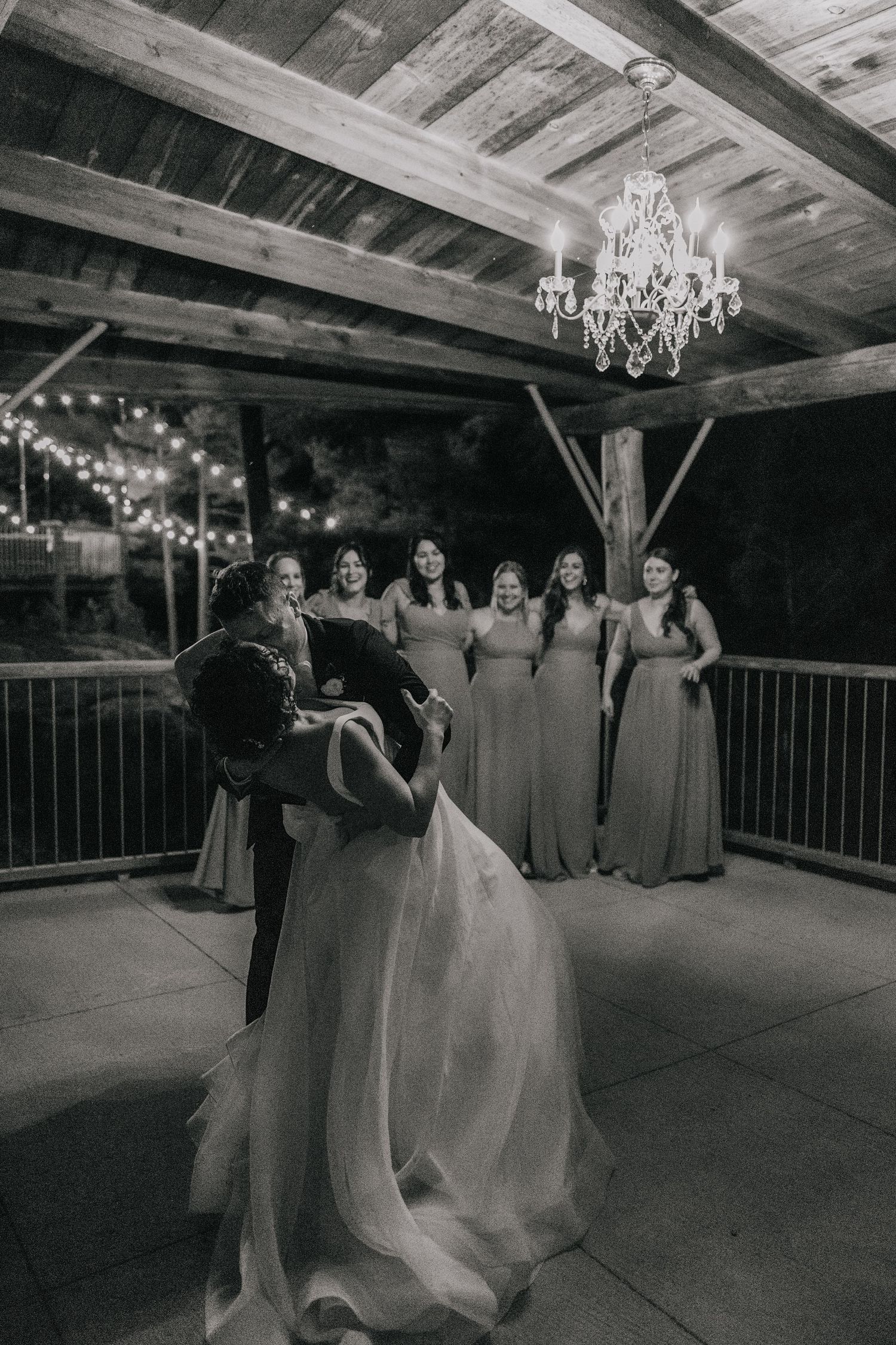 Wedding reception dance floor in a rustic barn venue with string lights and chandeliers creating romantic ambiance.