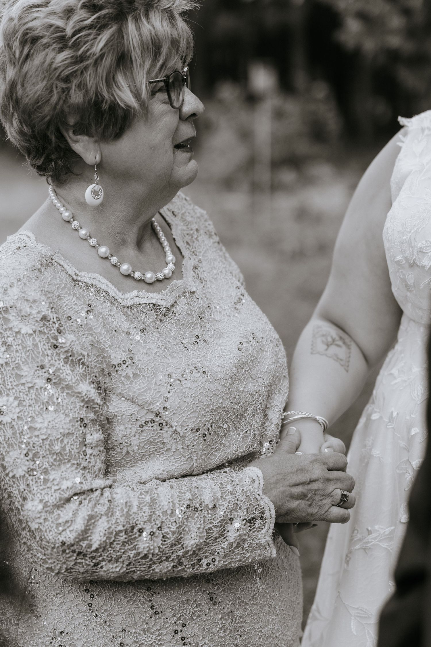 A touching black and white wedding moment showing an elegant woman in lace and pearls holding someone's arm tenderly.