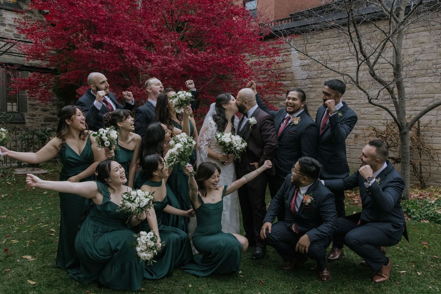 Wedding party poses together outdoors with bright red autumn foliage creating a vibrant backdrop.