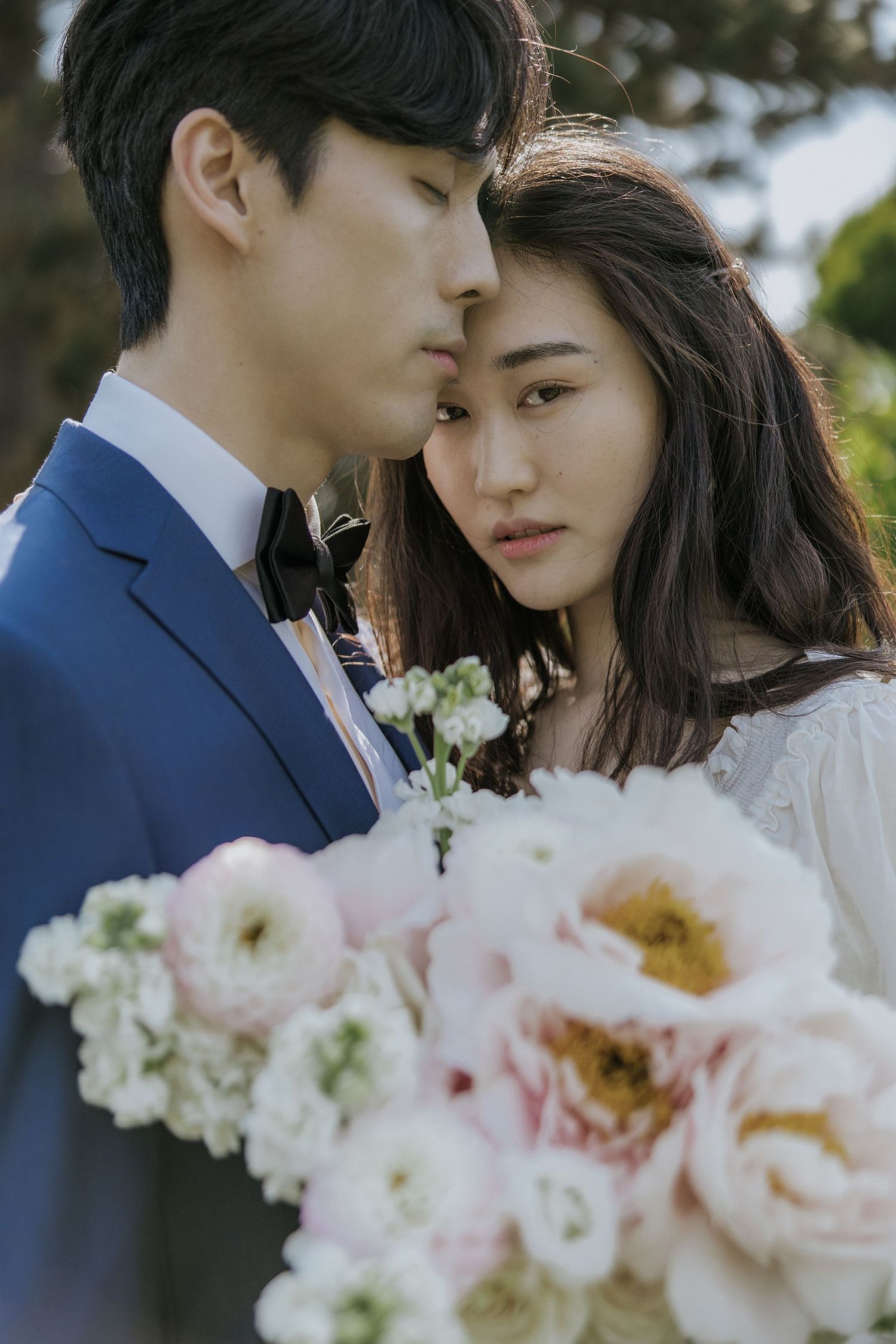 A romantic wedding couple shares intimate moments in a garden setting with soft pink and white floral bouquets.