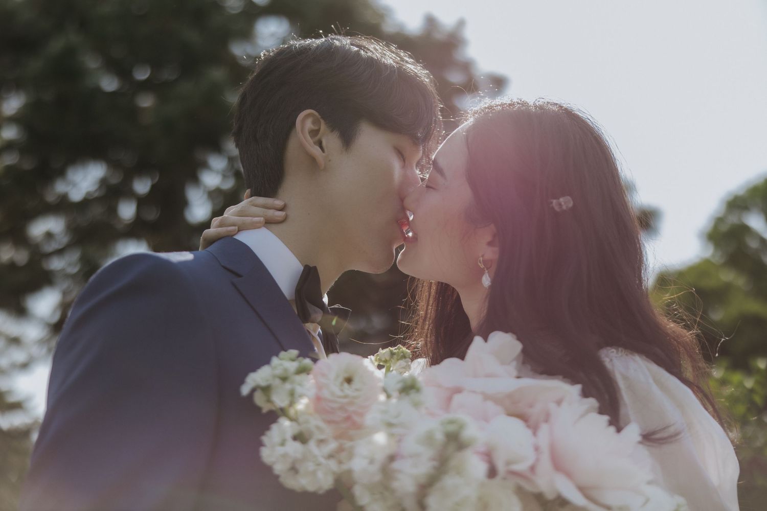 A romantic couple shares tender kisses surrounded by nature in a dreamy wedding photo series.