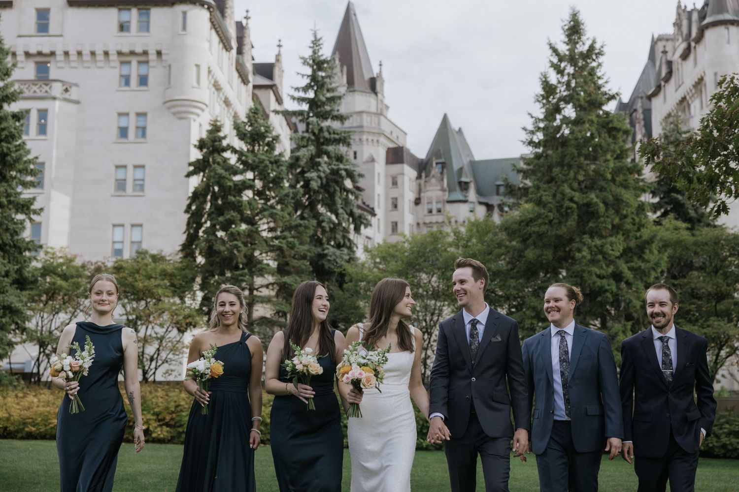 Wedding party in navy suits and dresses pose together on the grounds of a grand estate on an autumn day.