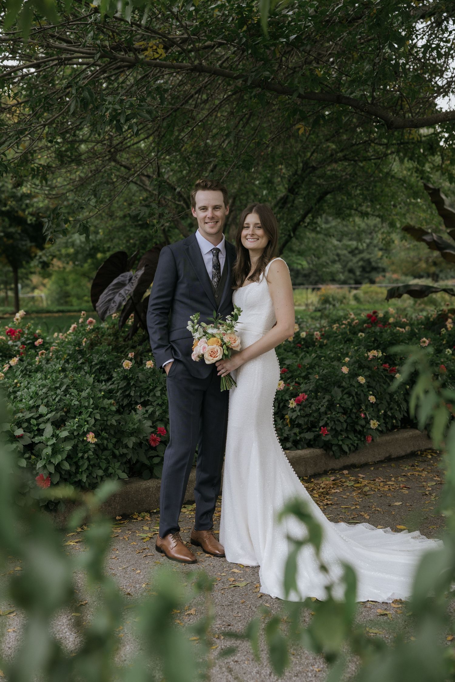 A couple shares a romantic moment in a lush garden setting with blooming roses and greenery.