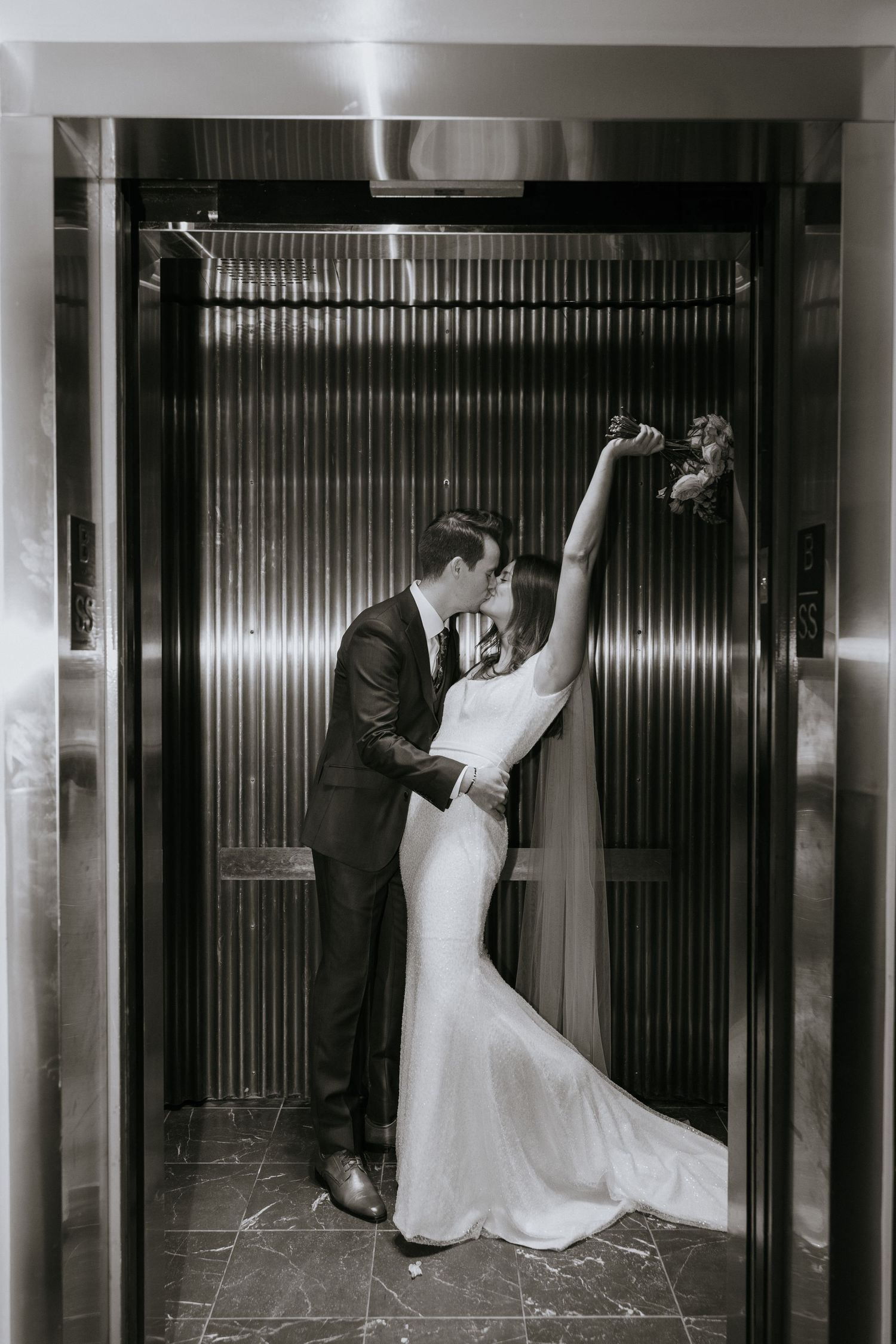 A romantic black and white wedding photo of a couple embracing in an elevator doorway.