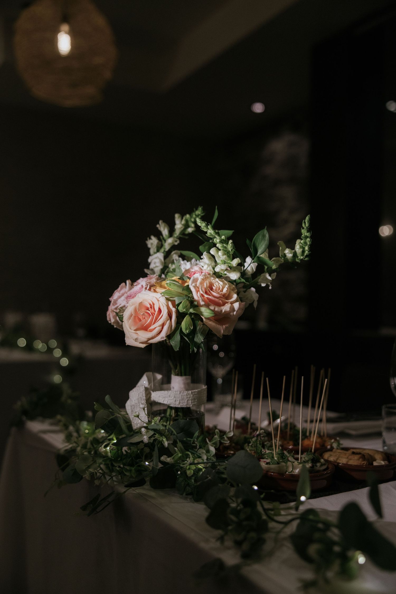 Elegant wedding table decorations with pink roses and greenery in moody lighting.