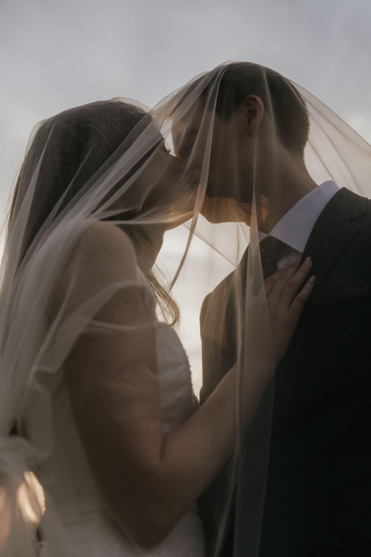 Romantic silhouette of a bride and groom sharing an intimate moment under a delicate veil during golden hour.