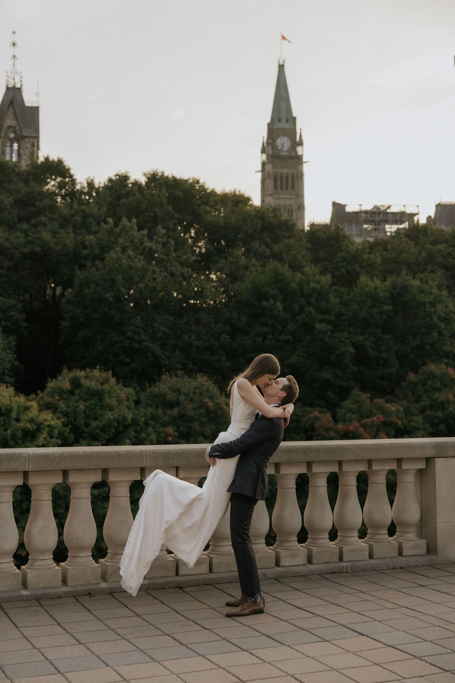 A romantic dip pose sequence of a couple dancing on a balcony with a historic cityscape and church spires in the background.