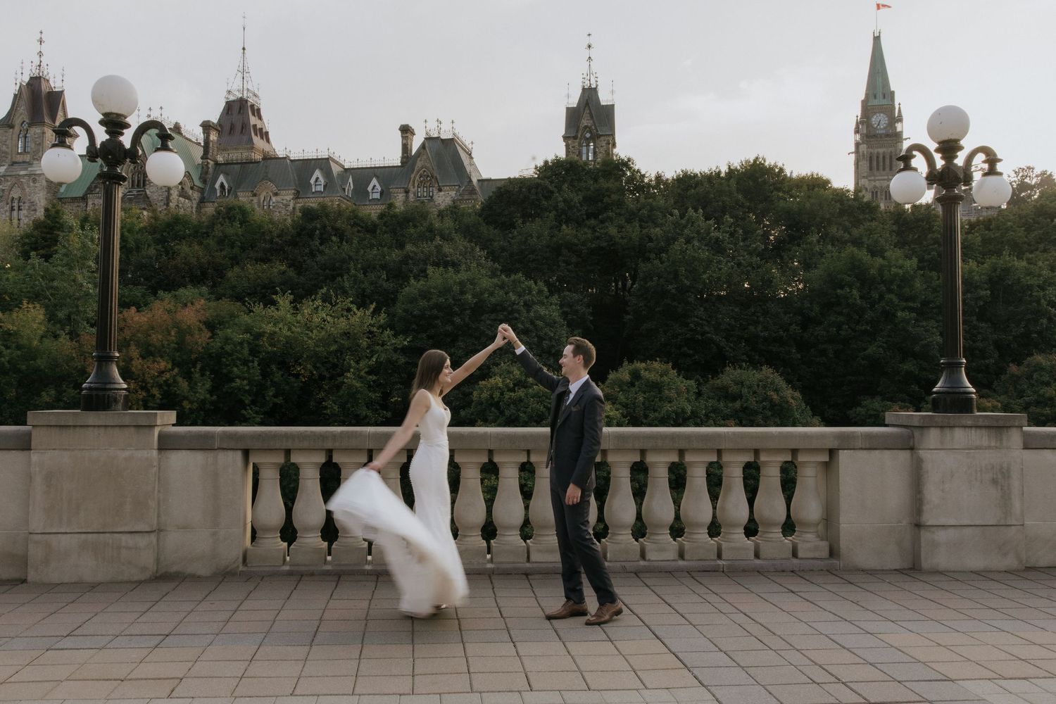 A couple dances on a terrace with historic architecture and spires visible in the background.