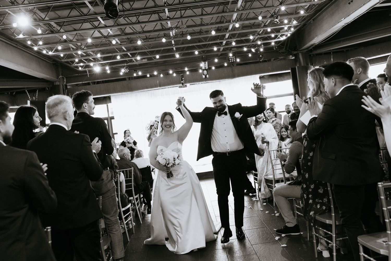 Wedding guests dance and celebrate on an illuminated dance floor under twinkling string lights at an evening reception.