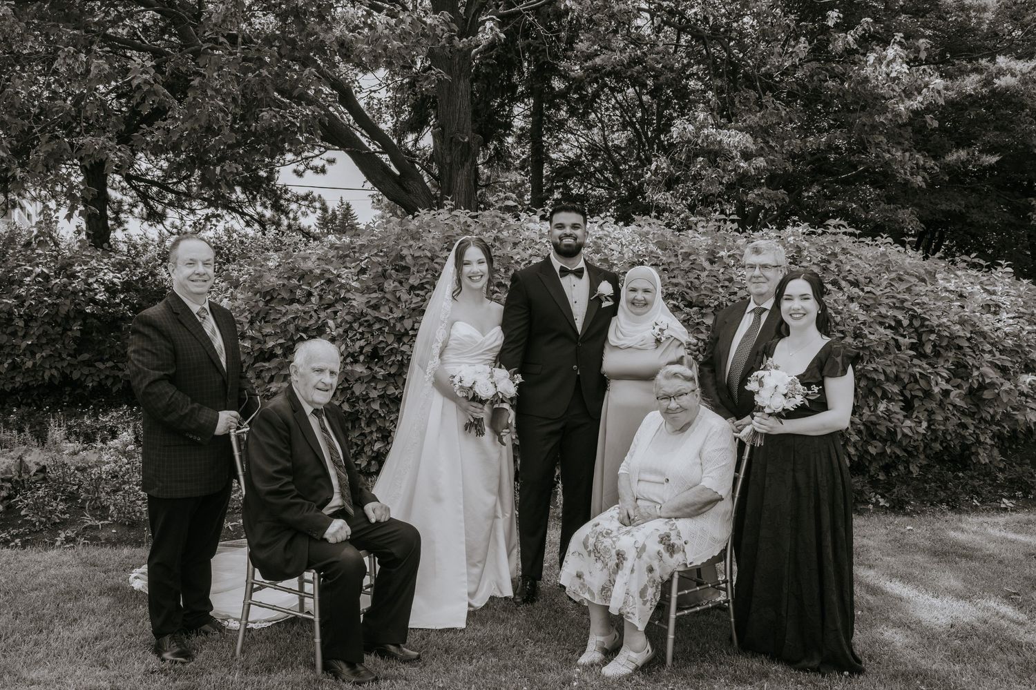 Wedding party members gather outdoors for candid photos in a garden setting.