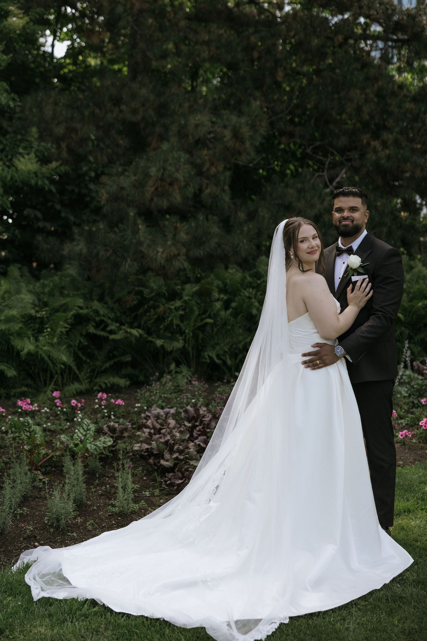 A romantic wedding photoshoot in a garden setting with flowing white dress and long veil trailing on grass.