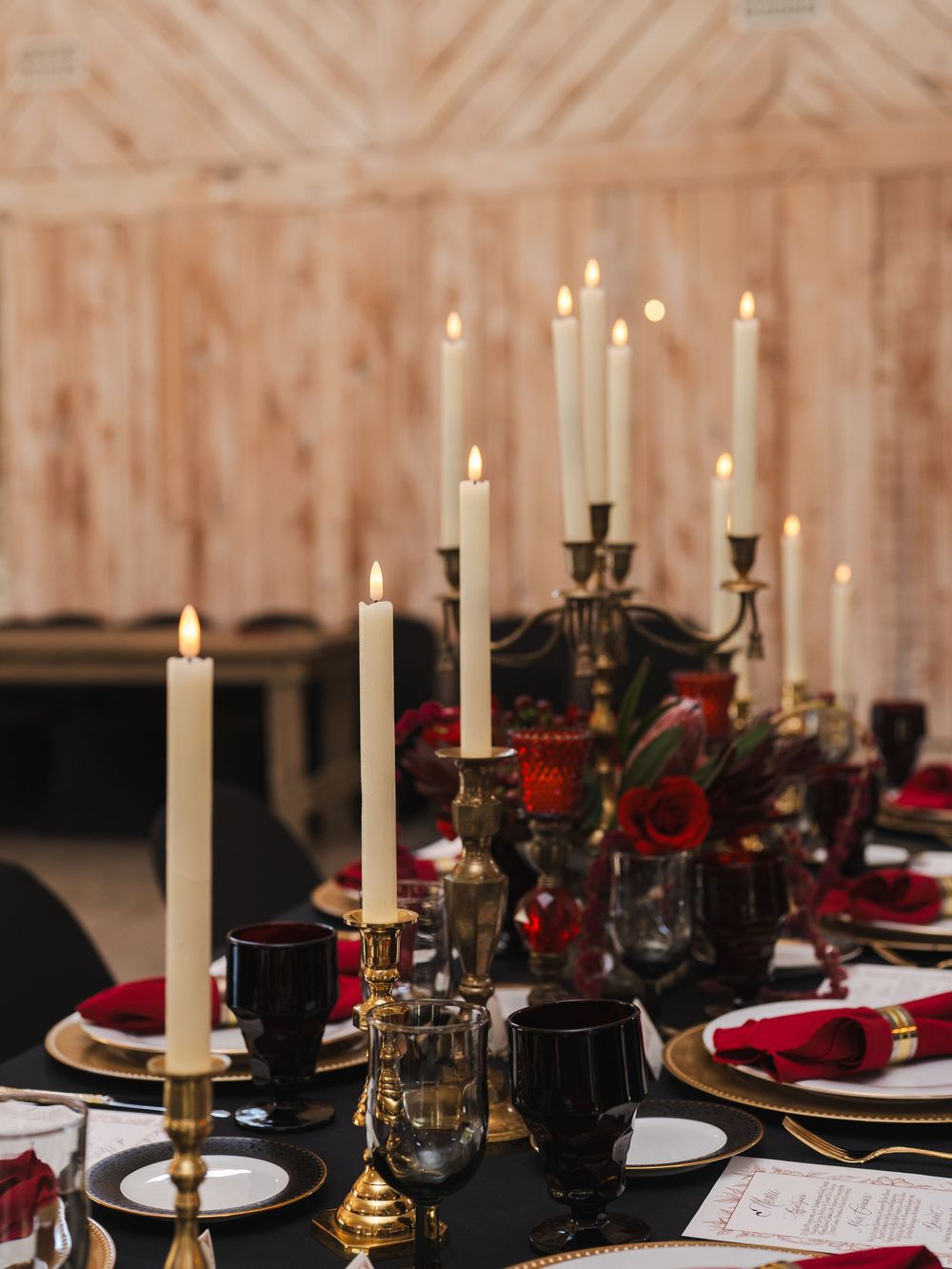 Romantic table setting with white taper candles, red roses, and black glassware for an elegant wedding reception.