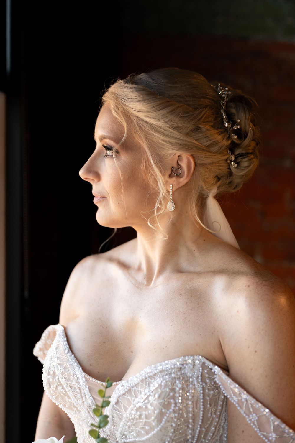Side profile of bride wearing a sparkling white strapless gown with delicate beading and drop earrings.