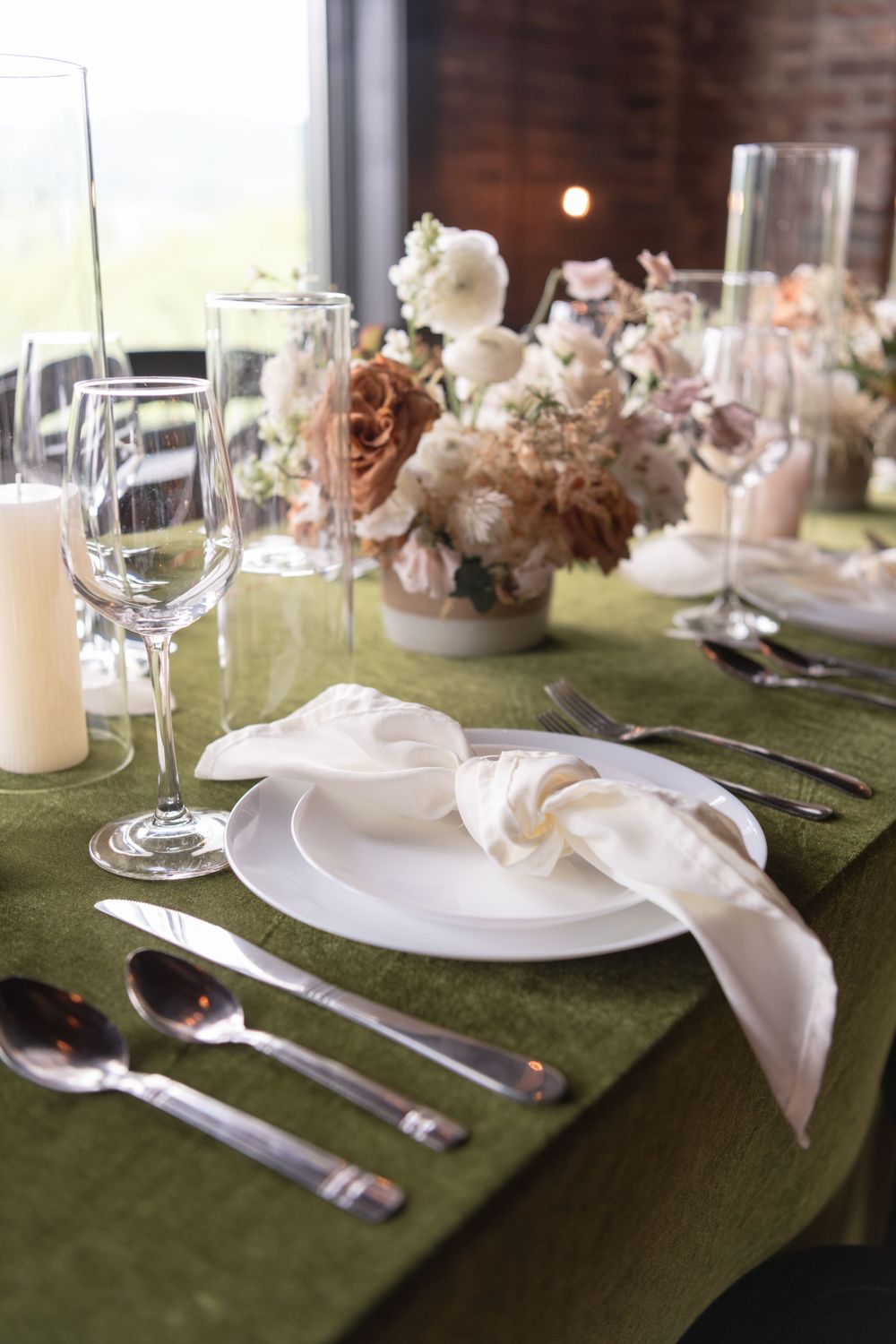 Elegant table setting with green linens, white plates and floral centerpiece.