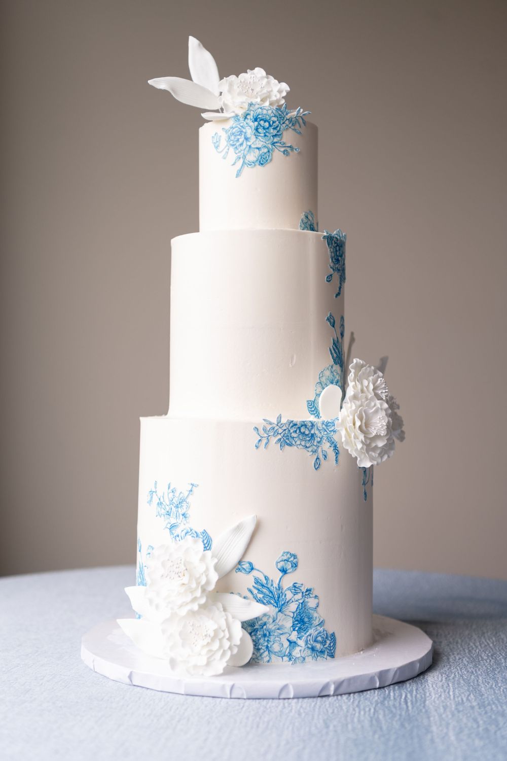 Three-tier white wedding cake decorated with blue accents and white sugar flowers.