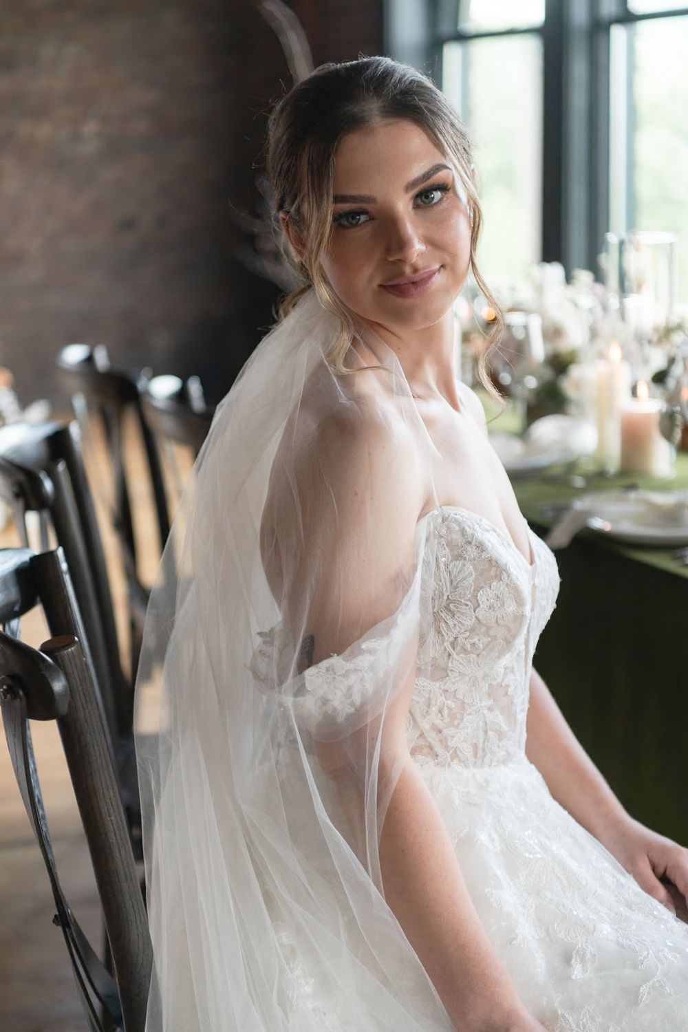 A bride in a romantic lace wedding gown sits beside industrial chic decor.